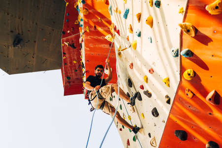 Man wearing belaying rope, climbing on a very high rock climbing wallの写真素材