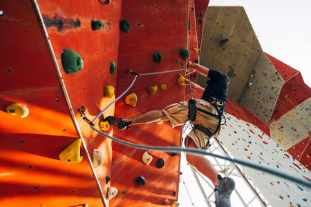 Man wearing belaying rope, climbing on a very high rock climbing wallの写真素材