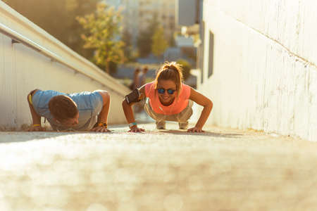 Couple in sportswear doing push-ups on the ground on urban placeの写真素材