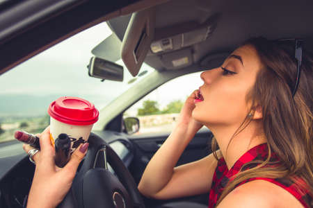 Young beautiful woman is in her car and enjoying doing make up using rearview mirrorの写真素材