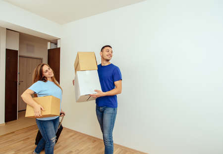 Happy young couple carrying cardboard boxes moving into new homeの写真素材