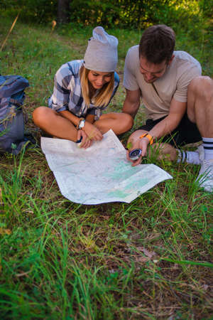 Young couple examining the map inside the forest. Hiking concept in the mountain in summerの写真素材
