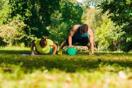Healthy young couple doing push-ups on grass into the parkの写真素材
