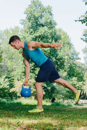 Attractive fitness instructor doing heavy weight exercise with kettlebell in the parkの写真素材