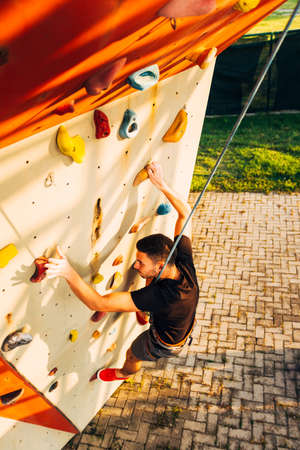 Man wearing belaying rope, climbing on a very high rock climbing wallの写真素材