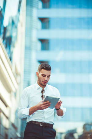 Cheerful business guy watching on his tablet while standing outdoorの写真素材