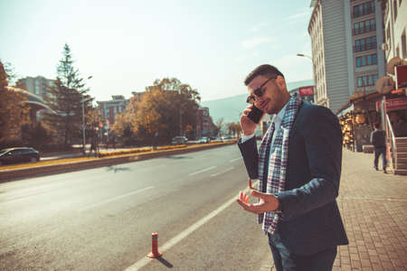 Young businessman is outdoors, having a call, while enjoying the view of the city and the beautiful weatherの写真素材