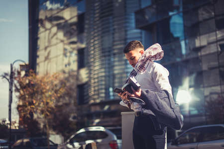 Young lawyer is standing outside on a windy day, the wind is blowing his scarf while he is holding his coffee and notebook in handsの写真素材