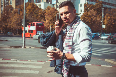 Man in suit is walking on the pedestrian crossing and having a conversation on his phone while holding a coffeeの写真素材