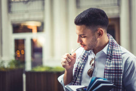 Young man wearing a white shirt is outside and he is lighting a cigaretteの写真素材
