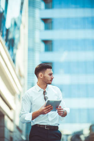 Caucasian businessman in white shirt holding tablet on sunny day outdoorの写真素材