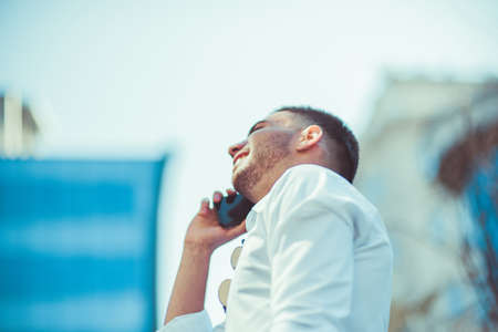 Caucasian businessman in white shirt talking on his cell phone on sunny day outdoorの写真素材