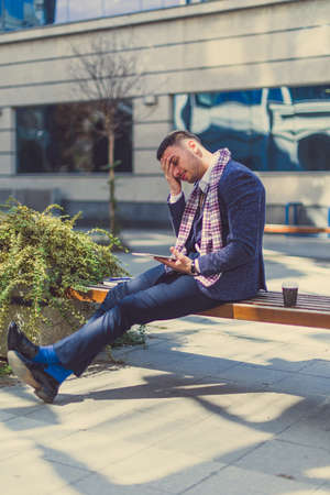 An urban guy is being nervous with his hand stick to his head, he is drinking coffee and looking at his tabletの写真素材