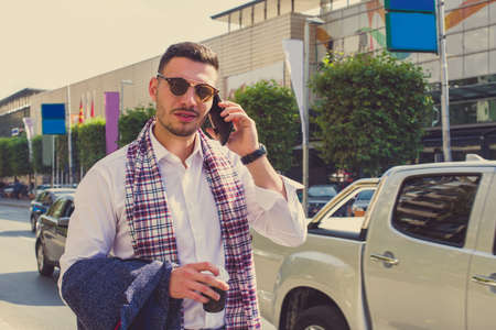 Young lawyer is enjoying the good weather and standing in front of the mall, holding coat and having a phone callの写真素材
