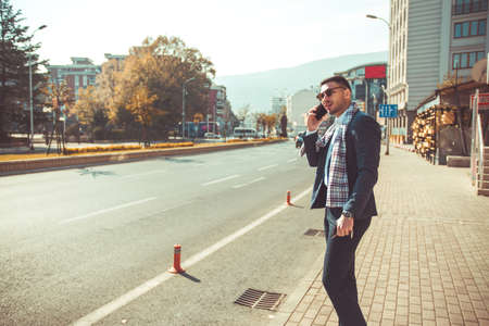 Stylish young man is arguing on his mobile phone while standing on the sidewalk on the streetの写真素材