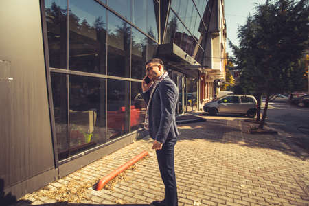 Urban businessman is standing on the sidewalk in front of a building and having a conversation on his phoneの写真素材
