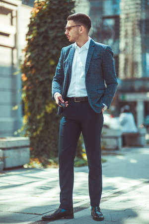 Confident businessman wearing a suit standing outdoors and holding his mobileの写真素材