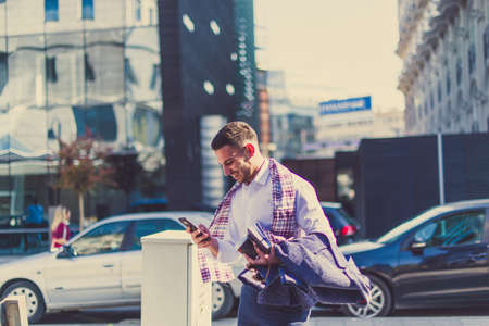 An urban businessman is outdoors, looking happy while loooking at his mobile phoneの写真素材