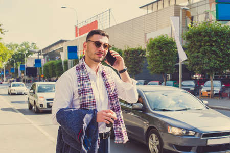 Successful businessman is making a phone call in the middle of the street in big city jar, he is holding coat in his hands and a coffee to goの写真素材