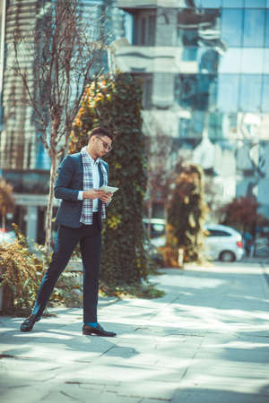 A businessman is holding his notebook and walking in the city square, enjoying the viewの写真素材