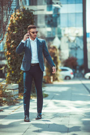A man in suit is on the city square, looking around him and talking to his mobile phoneの写真素材