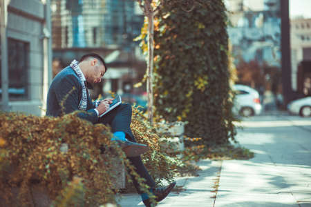 A man in suit is outdoors, enjoying the beautiful weather and writing at his notebookの写真素材