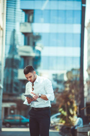 Caucasian businessman in white shirt holding tablet on sunny day outdoorの写真素材