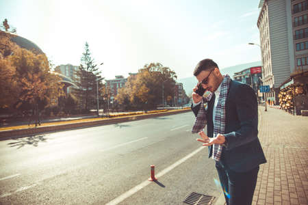 Stylish young businessman is arguing on his mobile phone while standing on the sidewalk on the streetの写真素材