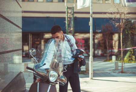An urban businessman is standing in the city center and looking in the parked motorcycleの写真素材