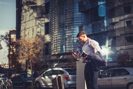 An urban businessman is outdoors, looking happy while loooking at his mobile phoneの写真素材