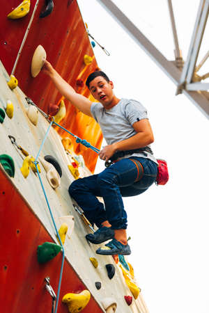 Young climber guy climbing on practical rock in climbing center, boulderingの写真素材