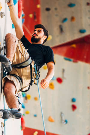 Man wearing belaying rope, climbing on a very high rock climbing wallの写真素材