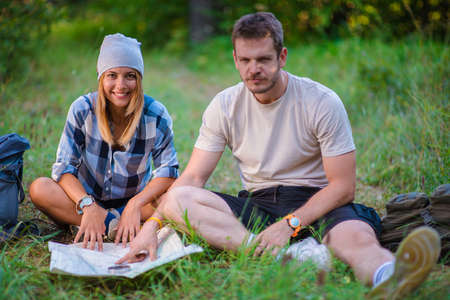 Young couple resting and checking the map inside the forest. Hiking concept in the mountain in summerの写真素材
