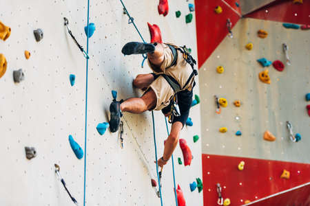 Man wearing belaying rope, climbing on a very high rock climbing wallの写真素材