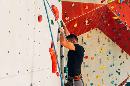 Young man climbs up an outdoors rock wallの写真素材