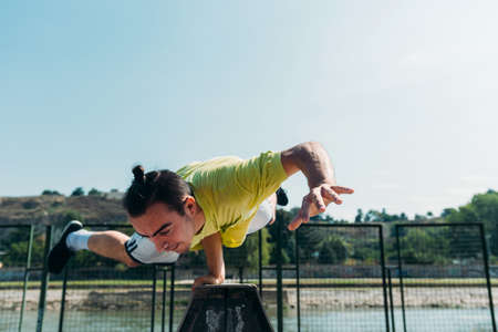Sporty man maintains a balance on pyramid with one hand in skatepark
