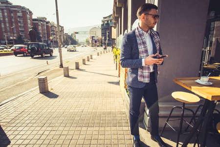A businessman is standing in the cafe and enjoying his coffee break while looking interested in the city jamの写真素材