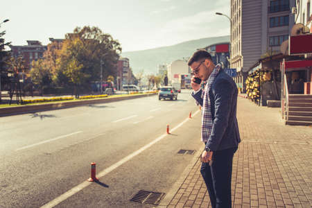 Young businessman is outdoors, having a call, while enjoying the view of the city and the beautiful weatherの写真素材