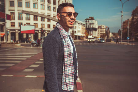 A modern young man with beautiful scarf and suit is standing in the city centerの写真素材