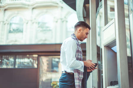 Young businessman is in the city, standing next to the automated teller machineの写真素材