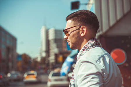 Stylish businessman is walking down the street in an urban city, looking in the beautiful buildings around himの写真素材
