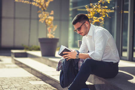An eloquent businessman is outside, he is enjoying in the beautiful weather while looking at the notebookの写真素材