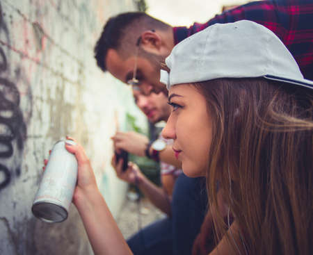 Three urban people are having fun together, drawing grafitii on the wall