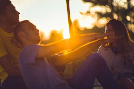 Three friends are enjoying beautiful sunset in the park, smiling and fooling aroundの写真素材