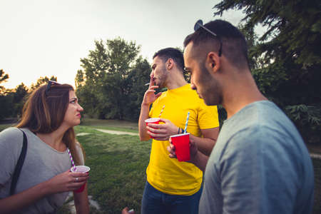 Three friends are outdoors having conversation while drinking coffee and smoking cigarettesの写真素材