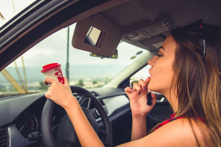 Young female is sitting in her car while is doing her makeup on the car mirrorの写真素材
