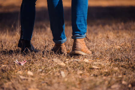 A beautiful, young couple in jeans and boots is standing close in the park