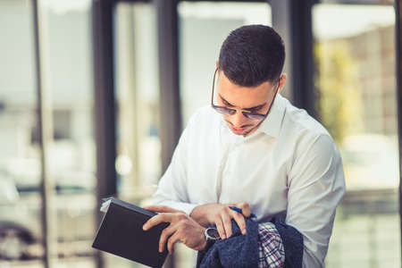 Modern businessman holding notes while looking in his watch while standing outsideの写真素材