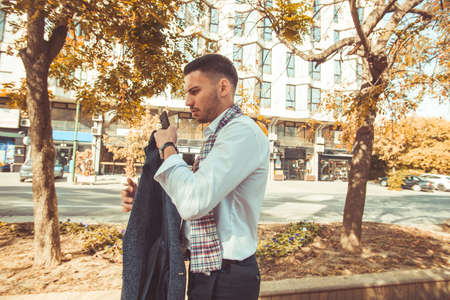A young businessman is walking in the city, looking serious while holding his coat and phone in handsの写真素材