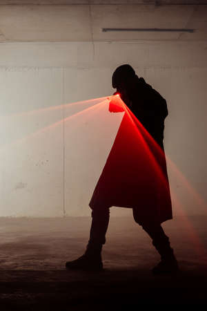 Silhouette of a man standing in a dark room and holding laser revolver